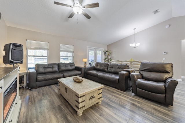 living room with french doors, ceiling fan with notable chandelier, dark wood-type flooring, and vaulted ceiling