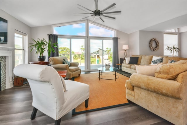 living room with ceiling fan, dark wood-type flooring, a tiled fireplace, and lofted ceiling