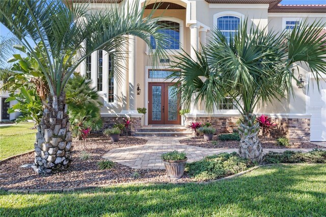 property entrance with stone siding, stucco siding, a lawn, and french doors