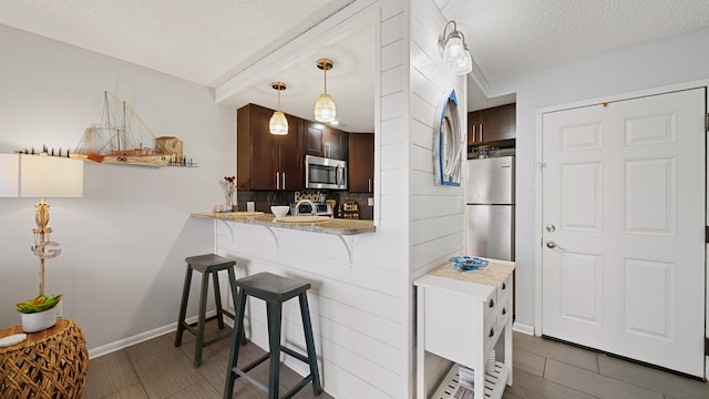 kitchen with stainless steel appliances, pendant lighting, a textured ceiling, a breakfast bar area, and dark brown cabinets