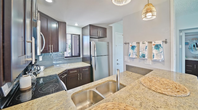 kitchen featuring light stone countertops, backsplash, dark brown cabinetry, stainless steel appliances, and sink