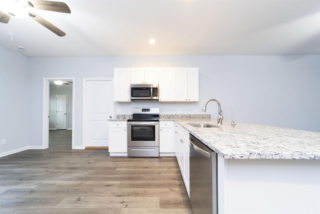 kitchen with sink, light stone countertops, appliances with stainless steel finishes, white cabinetry, and wood-type flooring