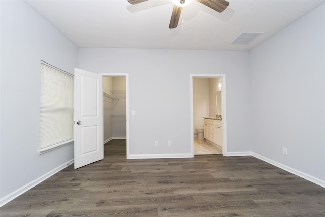 unfurnished bedroom featuring a spacious closet, ceiling fan, dark wood-type flooring, ensuite bathroom, and a closet