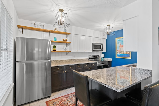 kitchen with light tile patterned floors, stainless steel appliances, light stone counters, white cabinets, and decorative light fixtures