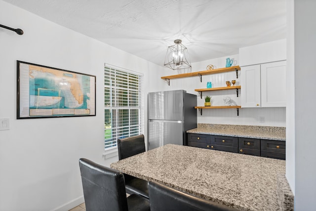 kitchen featuring stainless steel refrigerator, hanging light fixtures, light stone counters, white cabinets, and a chandelier