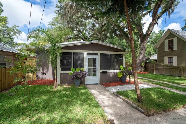 view of front of house with fence, stucco siding, a sunroom, and a front yard