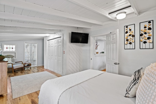 bedroom featuring beamed ceiling, baseboards, and light wood finished floors