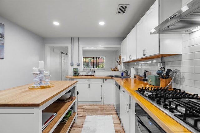 kitchen featuring wall chimney range hood, wooden counters, visible vents, a sink, and stainless steel appliances