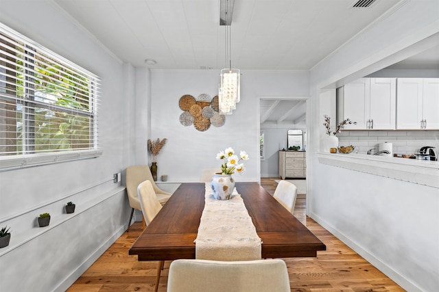 dining area featuring light wood-type flooring, baseboards, crown molding, and a notable chandelier