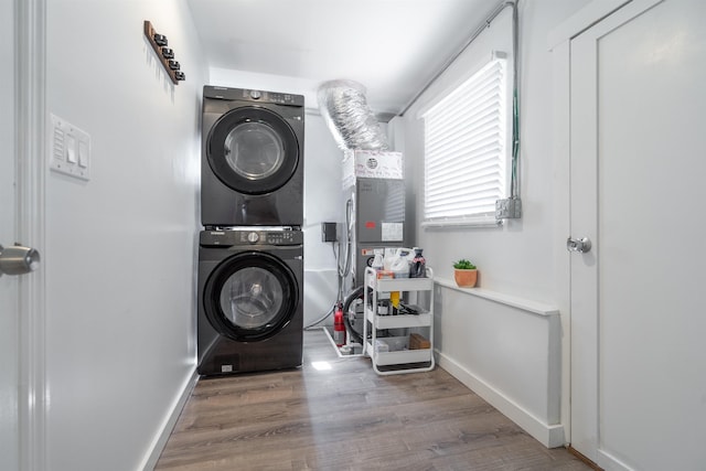 clothes washing area featuring baseboards, laundry area, stacked washing maching and dryer, and wood finished floors