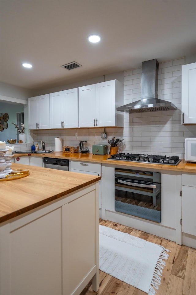 kitchen with visible vents, appliances with stainless steel finishes, butcher block counters, and wall chimney exhaust hood