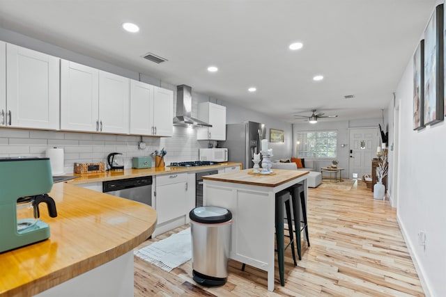kitchen with wall chimney range hood, ceiling fan, visible vents, wood counters, and stainless steel appliances