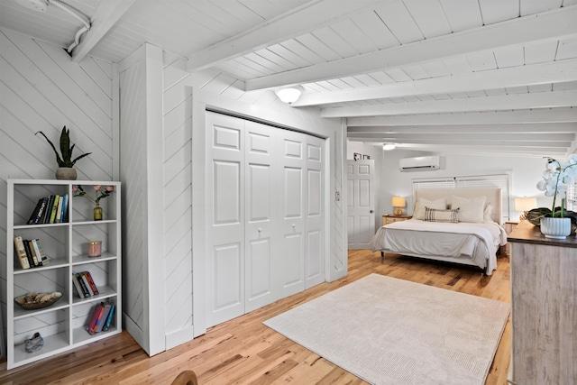 bedroom featuring light wood-style floors, a wall mounted air conditioner, beamed ceiling, wood ceiling, and a closet