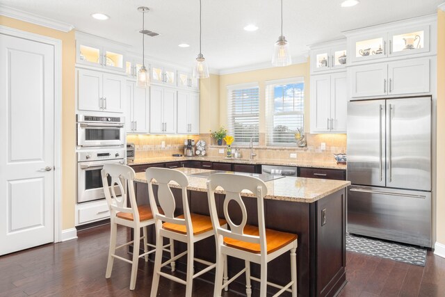 kitchen featuring a kitchen bar, stainless steel appliances, white cabinetry, a kitchen island, and hanging light fixtures