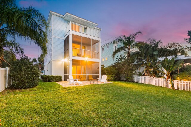 back house at dusk featuring a patio, a balcony, and a lawn