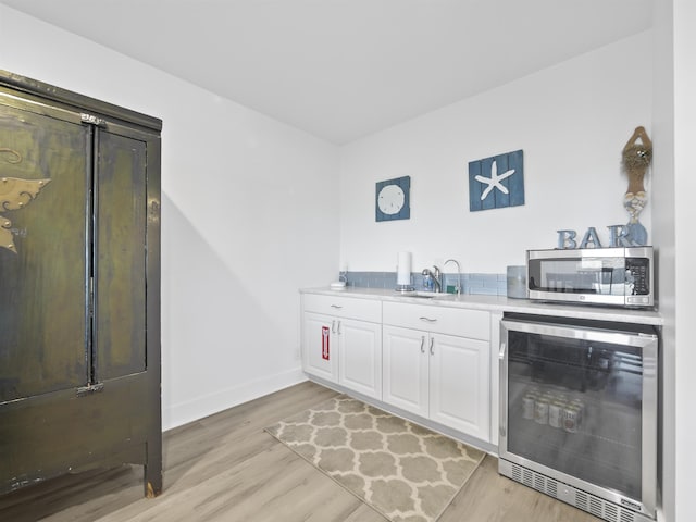 bar with sink, white cabinetry, light wood-type flooring, and wine cooler