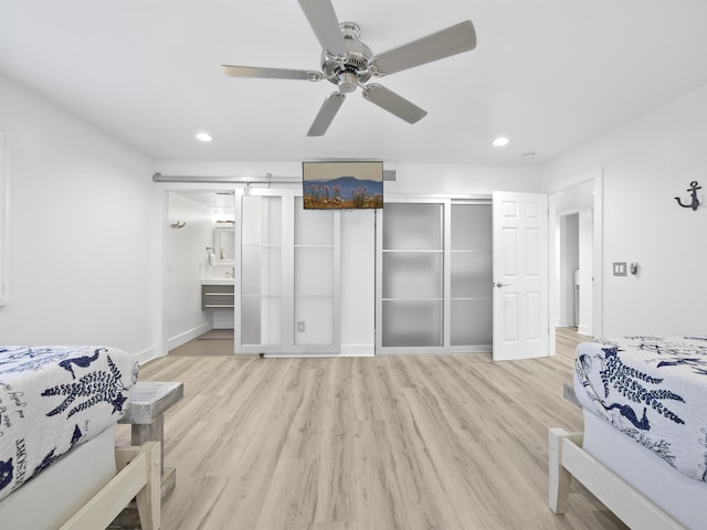 bedroom featuring ceiling fan, a barn door, light wood-type flooring, and connected bathroom