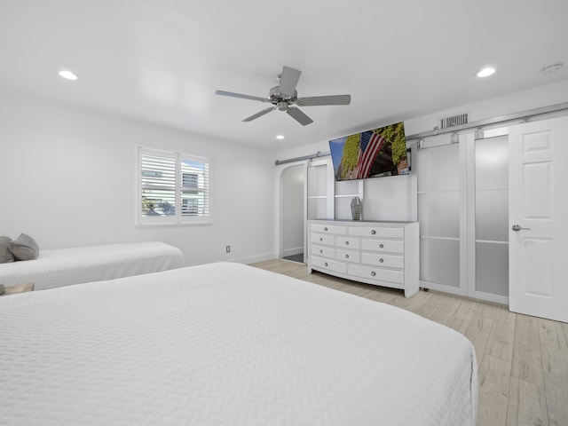 bedroom featuring ceiling fan, light hardwood / wood-style flooring, and a barn door