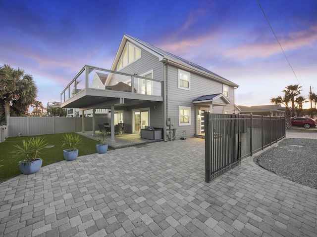 back house at dusk featuring a patio area, a lawn, and a balcony