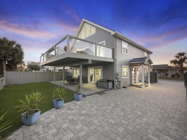 back house at dusk with a balcony, a yard, and a patio