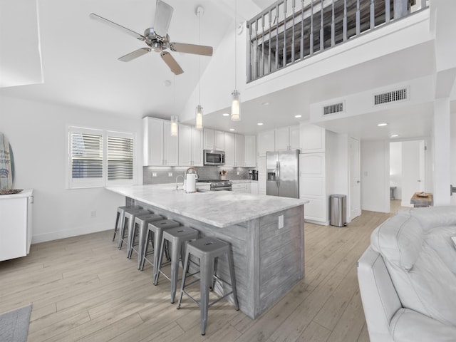 kitchen featuring white cabinetry, stainless steel appliances, hanging light fixtures, high vaulted ceiling, and a breakfast bar area