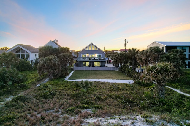 back house at dusk featuring a lawn