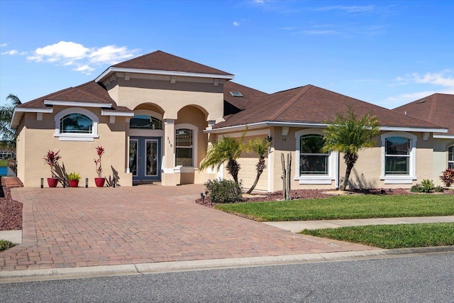 mediterranean / spanish-style home featuring a garage, decorative driveway, french doors, a front lawn, and stucco siding