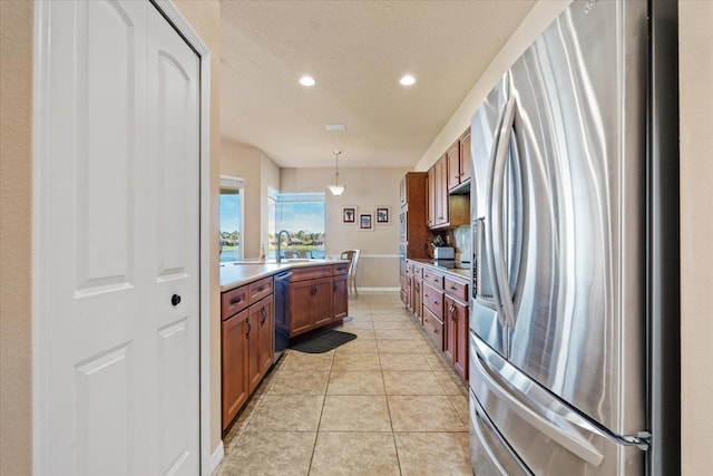 kitchen featuring brown cabinets, light countertops, stainless steel appliances, a sink, and light tile patterned flooring