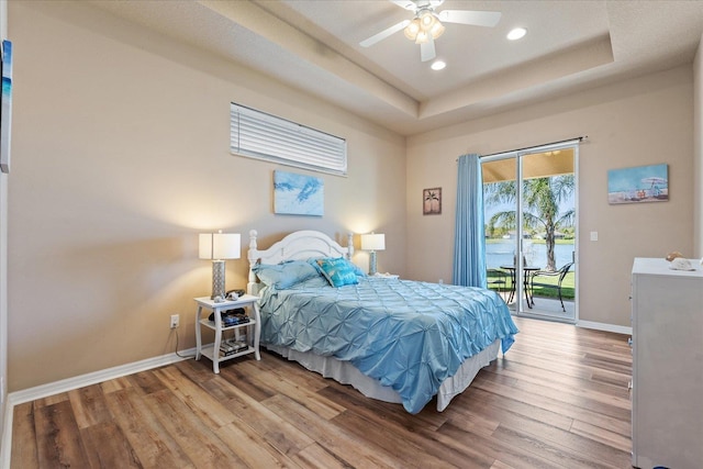 bedroom with recessed lighting, wood finished floors, baseboards, access to exterior, and a raised ceiling