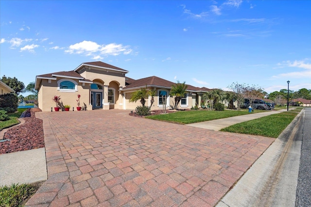 mediterranean / spanish house featuring a front lawn, decorative driveway, and stucco siding