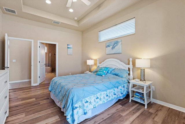 bedroom featuring baseboards, visible vents, a raised ceiling, and wood finished floors