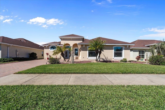 mediterranean / spanish-style house with stucco siding, decorative driveway, and a front yard