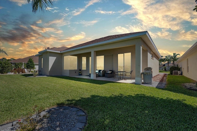 back of property at dusk with a yard, a patio, and stucco siding