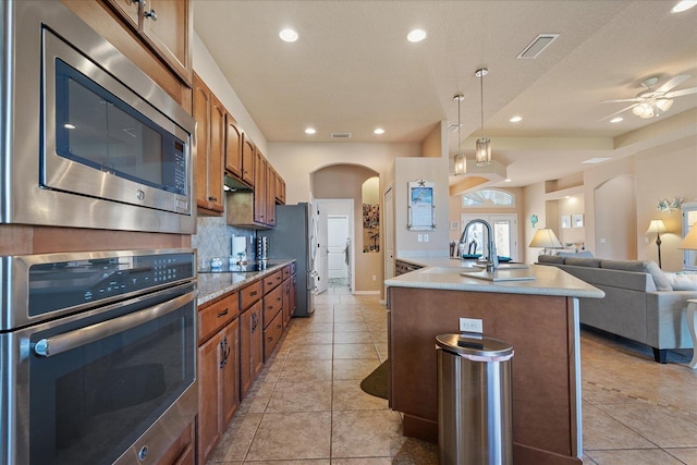 kitchen featuring visible vents, arched walkways, brown cabinets, open floor plan, and stainless steel appliances