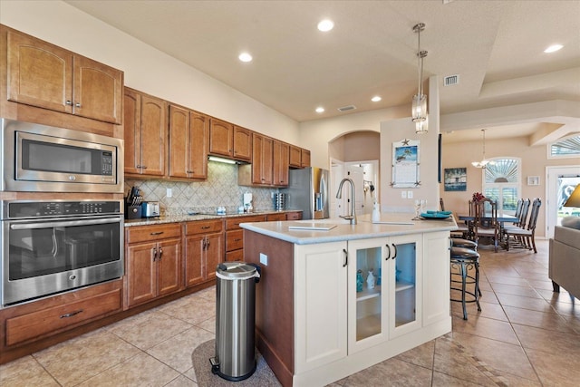 kitchen featuring a kitchen island with sink, stainless steel appliances, visible vents, tasteful backsplash, and brown cabinetry