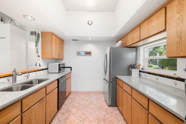 kitchen with sink, stainless steel appliances, light stone countertops, light tile patterned flooring, and a raised ceiling