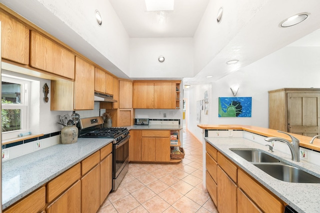 kitchen with a towering ceiling, sink, light tile patterned floors, light stone counters, and stainless steel gas range