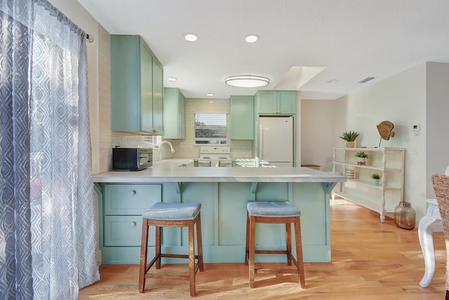 kitchen with kitchen peninsula, sink, white refrigerator, light hardwood / wood-style flooring, and a breakfast bar area