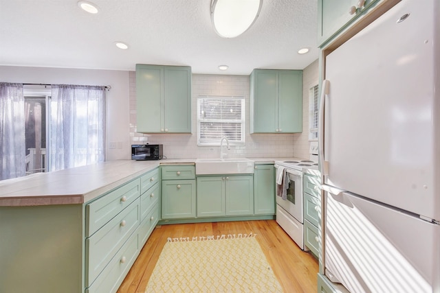 kitchen featuring white appliances, green cabinets, tasteful backsplash, light hardwood / wood-style floors, and kitchen peninsula