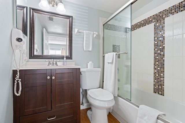 bathroom with visible vents, toilet, wood finished floors, shower / bath combination with glass door, and vanity