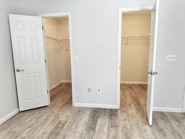 unfurnished bedroom featuring a walk in closet, a closet, and wood finished floors