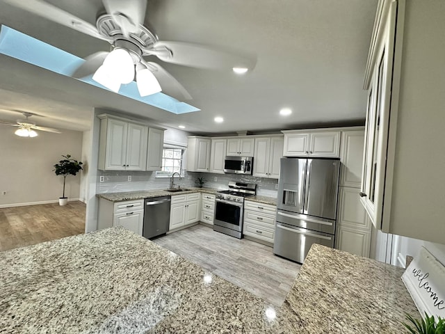 kitchen featuring a sink, decorative backsplash, appliances with stainless steel finishes, and a skylight