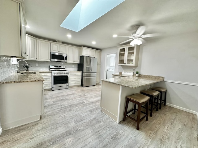 kitchen featuring a sink, appliances with stainless steel finishes, a peninsula, a skylight, and light stone countertops