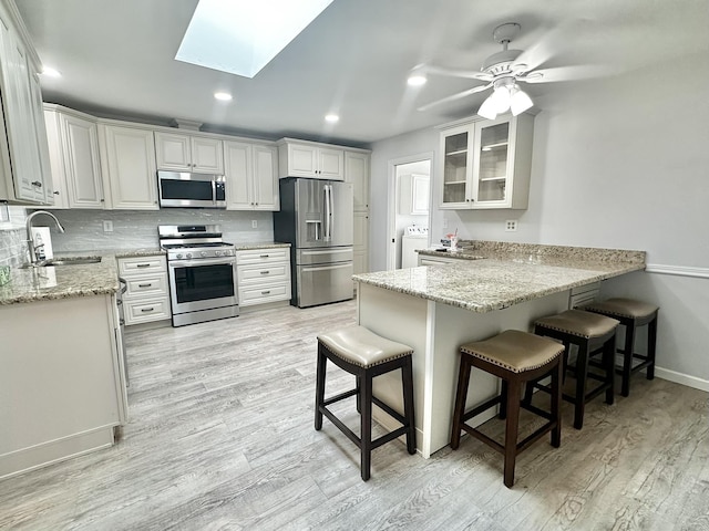 kitchen with decorative backsplash, washer / dryer, a peninsula, stainless steel appliances, and a sink