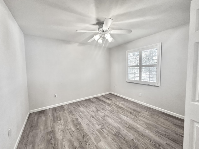 empty room with dark wood finished floors, a ceiling fan, and baseboards