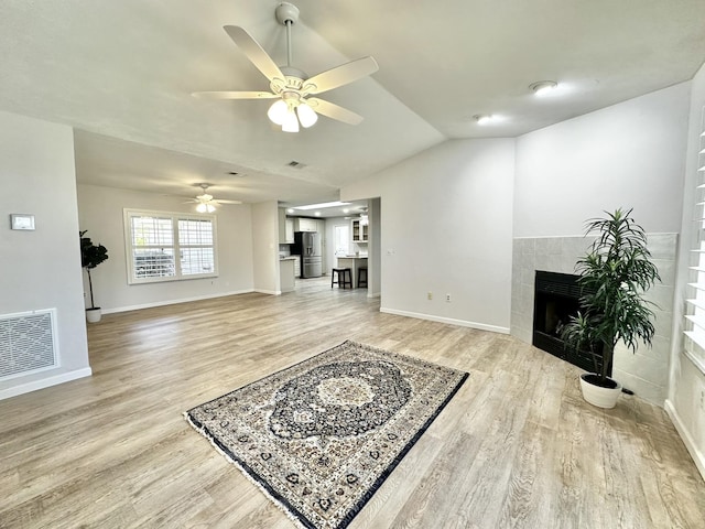 living area featuring visible vents, baseboards, vaulted ceiling, a tile fireplace, and light wood-style floors