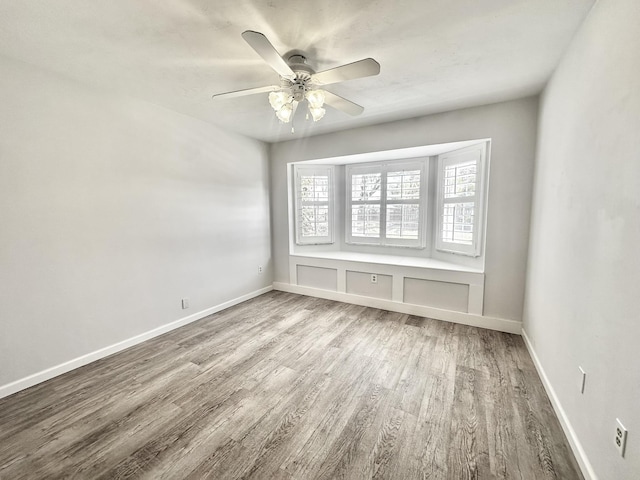 empty room with baseboards, wood finished floors, and a ceiling fan