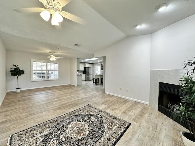 living area featuring a tiled fireplace, baseboards, light wood-type flooring, and lofted ceiling