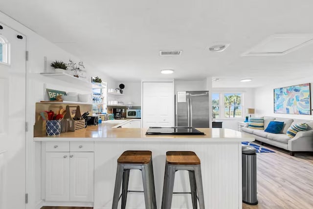 kitchen featuring stainless steel refrigerator, white cabinetry, kitchen peninsula, a kitchen bar, and black stovetop