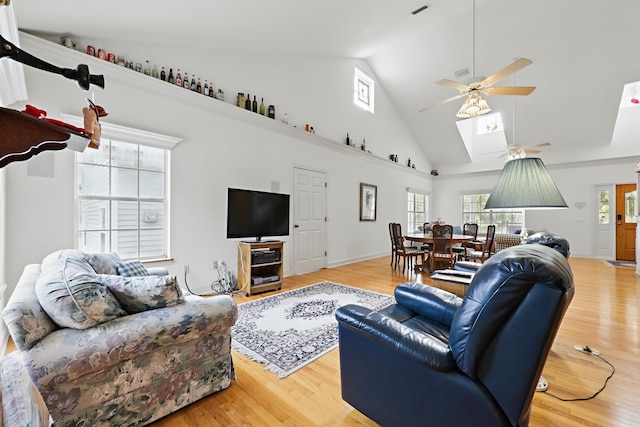 living area featuring a skylight, light wood-style flooring, high vaulted ceiling, and ceiling fan